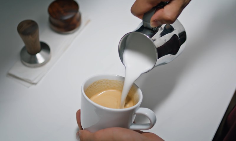 Osoba sipa mleko u šolju kafe